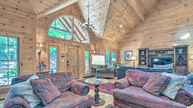 A log cabin interior with two patterned sofas, a round table, and a television in a wooden entertainment center.