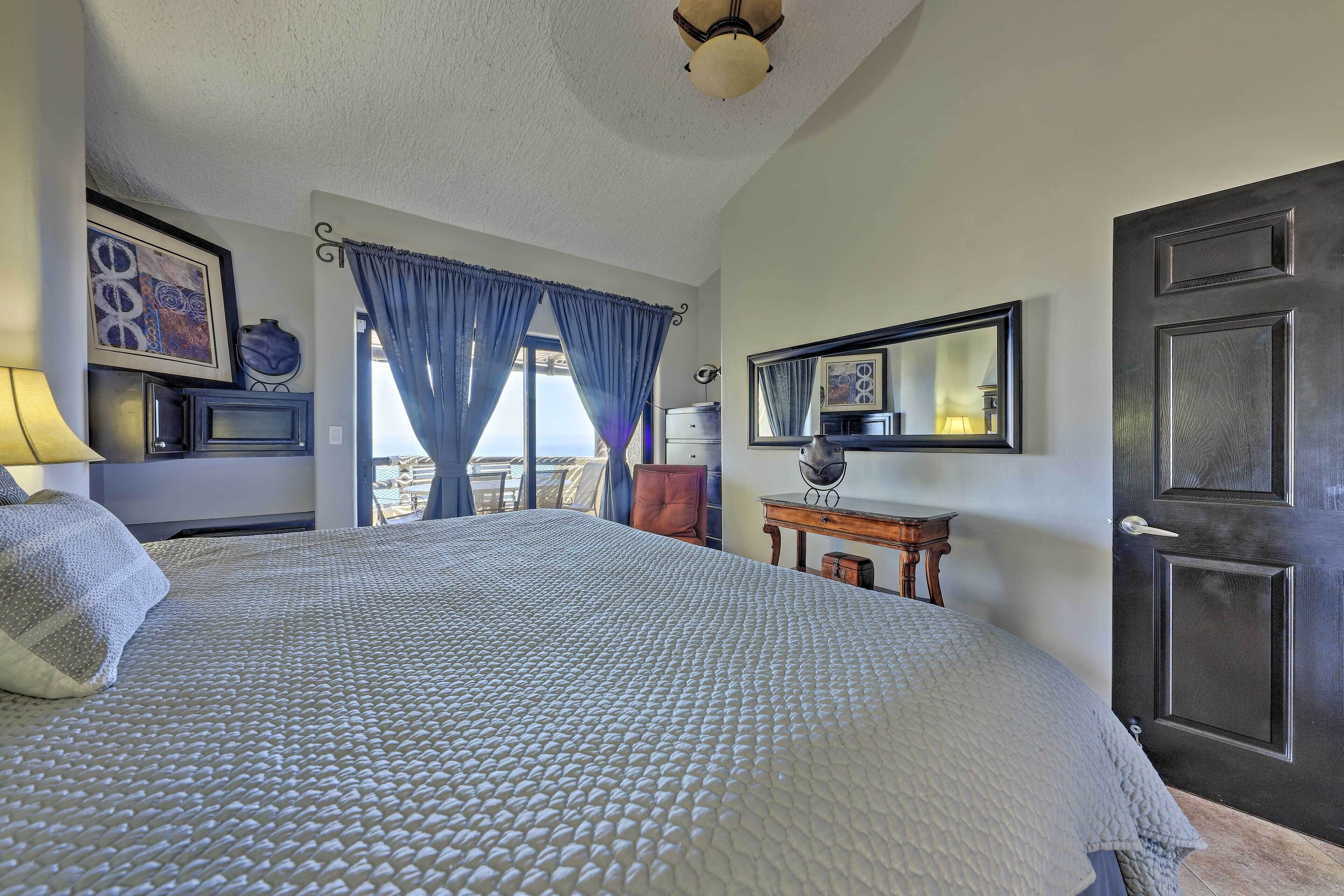 A bedroom with a large bed, a dresser, a chair, a desk, a mirror, and a door.