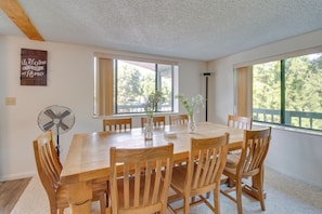 Un comedor con una mesa y sillas de madera, un ventilador y una ventana con vistas a árboles.