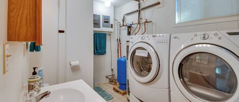 A laundry room with stacked washers and dryers, a sink with a faucet, and a blue water heater.