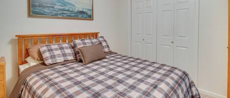 A bedroom with a wooden bed, a painting of a coastal scene, and a white door.