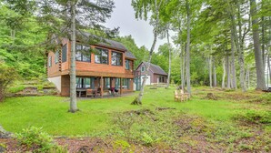 A wooden cabin with a large deck and a separate building, surrounded by a forest. - Lakefront Maine Retreat w/ Deck, Dock & Fire Pit! (Greenville)