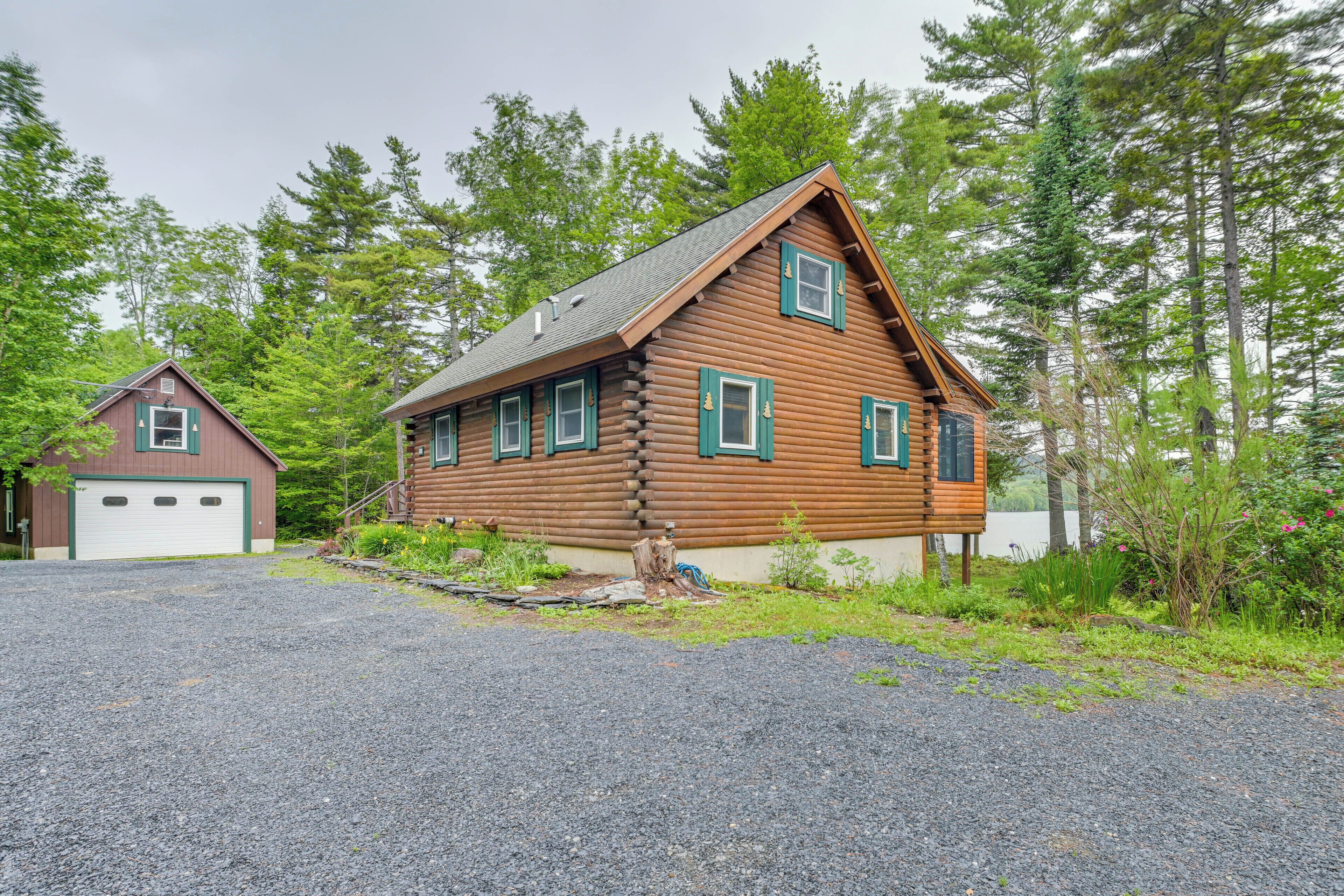 A log cabin with a garage, surrounded by dense forest.