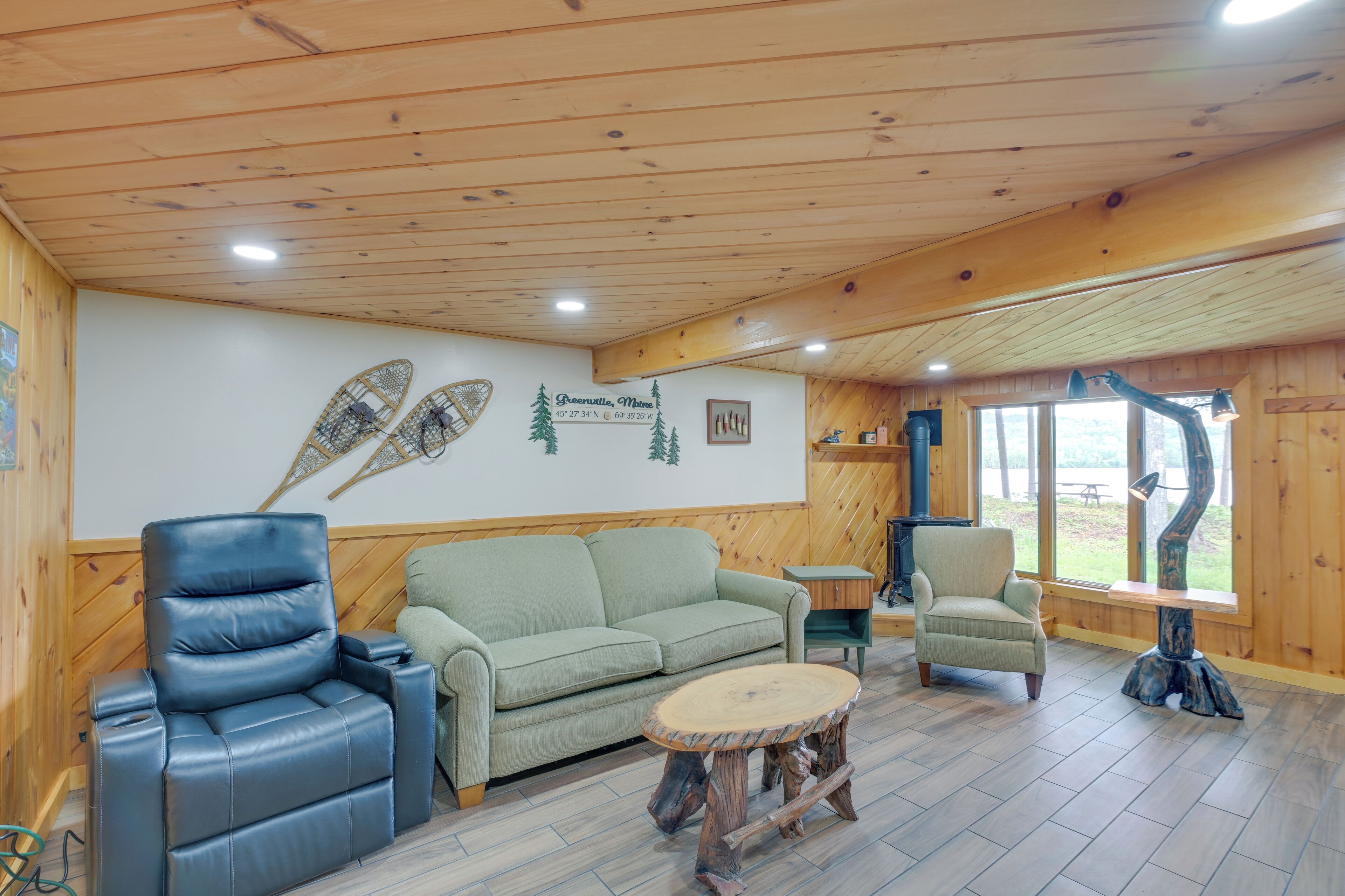 A cozy room with a wooden ceiling, a green sofa, a leather recliner, and a round wooden table.