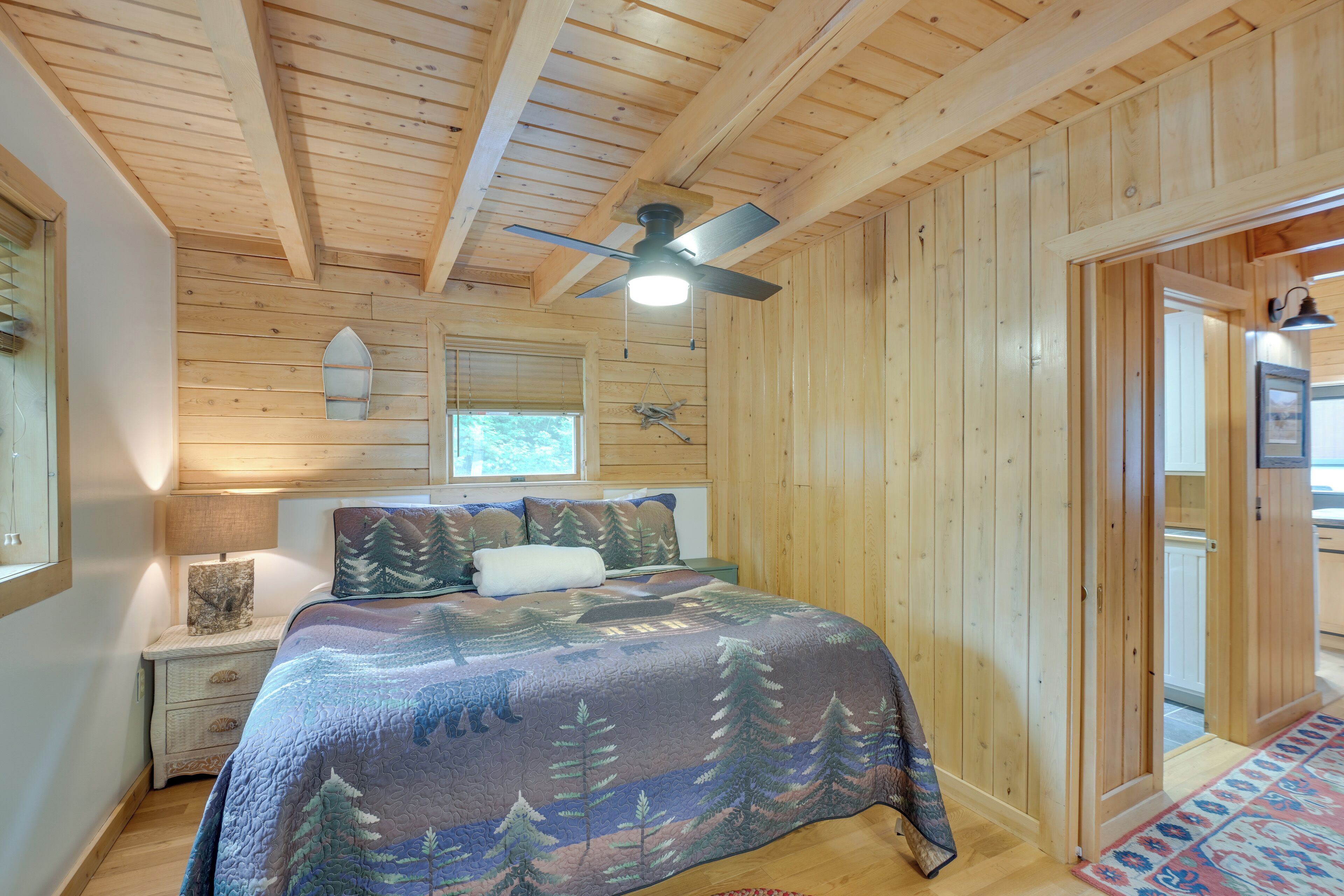 Ein Schlafzimmer einer Holzhütte mit Bett, Deckenventilator, Nachttisch und Fenster.