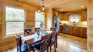 A wooden cabin interior with a dining area, kitchen, and large windows. - Family-friendly Murphy Cabin w/ Fire Pit! (Murphy)