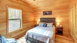 A wooden cabin bedroom with a bed, two bedside tables, a window, and a bear painting on the wall. - Family-friendly Murphy Cabin w/ Fire Pit! (Murphy)