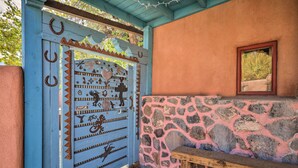 A rustic entrance with a blue door adorned with various symbols and designs, leading to a stone wall and a wooden bench.