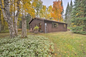 A cabin with a wooden exterior, surrounded by a forest with autumn-colored trees.