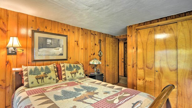 A wooden-paneled room with a bed, a framed picture on the wall, and a nightstand with a lamp.