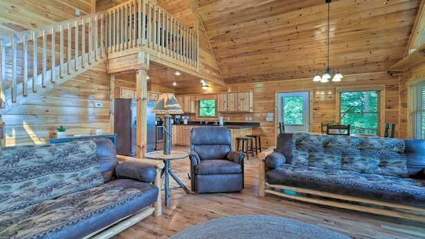 A spacious log cabin interior with a wooden staircase, a dining area, and a living room furnished with sofas and a chair. - Hiwassee Hideaway' Cabin w/ Mountain Views! (Murphy)