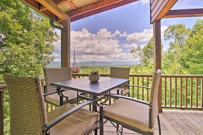A covered outdoor seating area with wicker chairs and a table, overlooking a scenic landscape with trees and mountains. - Hiwassee Hideaway' Cabin w/ Mountain Views! (Murphy)