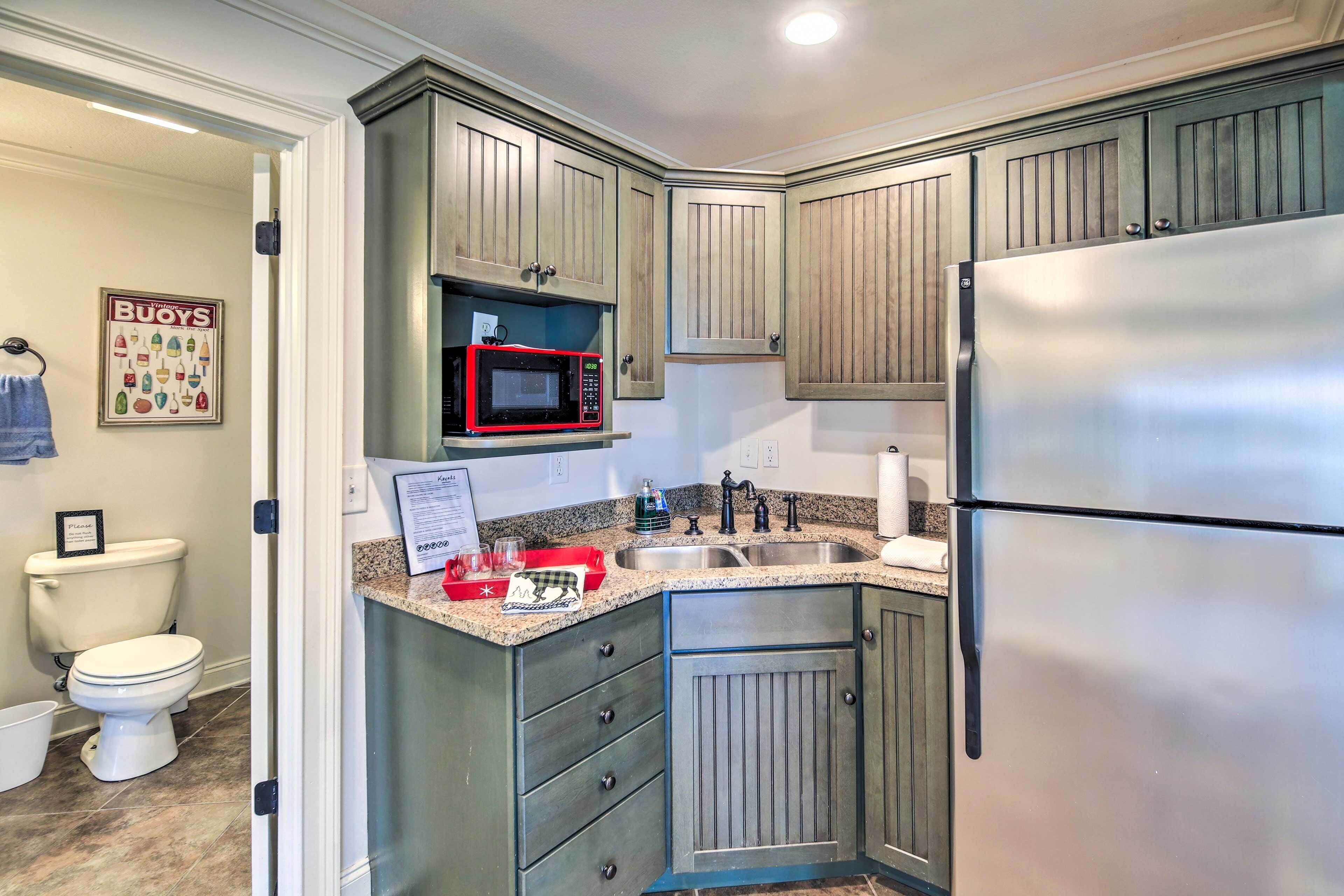 A compact kitchen with a stainless steel refrigerator, a microwave, and granite countertops.