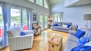A spacious living room with large windows, a grey sofa, a striped armchair, and a chessboard on a wooden chest. - Waterfront Piney Flats Home w/ Private Dock! (Piney Flats)