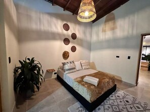 Een slaapkamer met een bed, een hanglamp, een plant in pot en een wand met decoratieve borden.