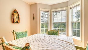Een kamer met een groot raam, een tafel met een bloemrijk tafelkleed en een stoel met een groene kussenzak.