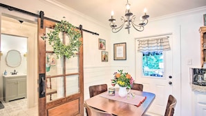 A dining area with a wooden table, chairs, a chandelier, and a window with curtains. - Charming Country Cottage: 5 Mi to Downtown Tulsa! (Tulsa)