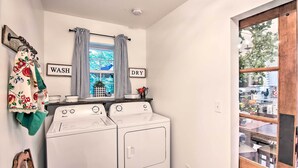 A laundry room with two white front-loading washers and dryers, a window with striped curtains, and a sign above the window that reads "WASH" and "DRY". - Charming Country Cottage: 5 Mi to Downtown Tulsa! (Tulsa)