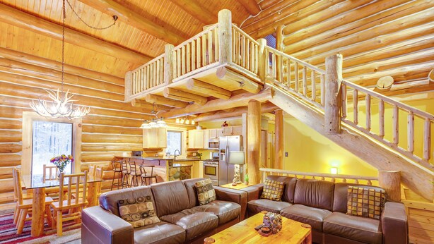 L’intérieur d’une cabane en rondins, avec un escalier en bois, des canapés en cuir, un coin repas et une cuisine.