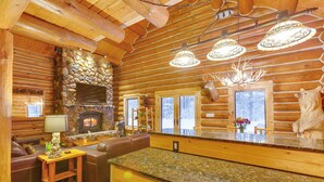 L’intérieur d’une cabane en rondins, avec une cheminée en pierre, des poutres en bois au plafond et un mur en pierre.