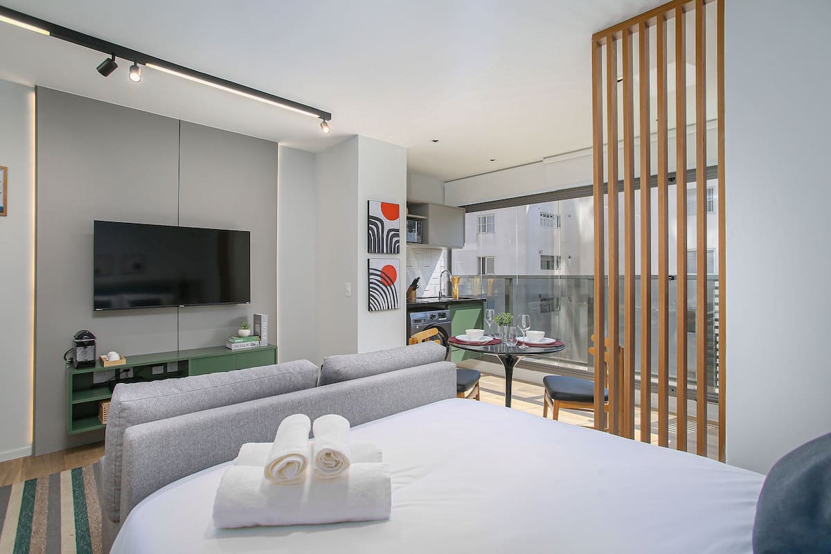 Une chambre d’hôtel moderne équipée d’un lit, d’une télévision à écran plat, d’un coin repas avec une table et des chaises, et d’un balcon avec vue.