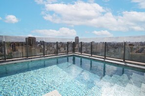A rooftop swimming pool with a cityscape view, surrounded by a glass barrier.