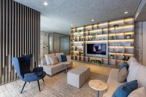 A modern living room with a sofa, chairs, a TV, and a wall-mounted shelf with plants and decor.
