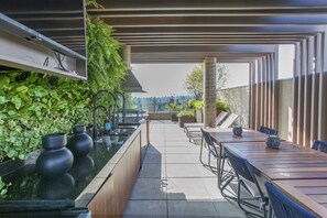 A rooftop terrace with a long wooden table, chairs, and a black countertop with two vases. - DSG Itaim (São Paulo)