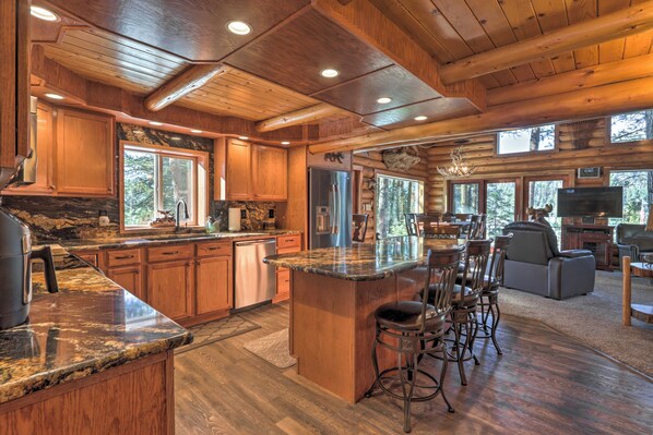 A spacious kitchen with wooden cabinets, granite countertops, and a large island with bar stools. - Cascade Cabin w/ Mountain View & River Access (Cascade)
