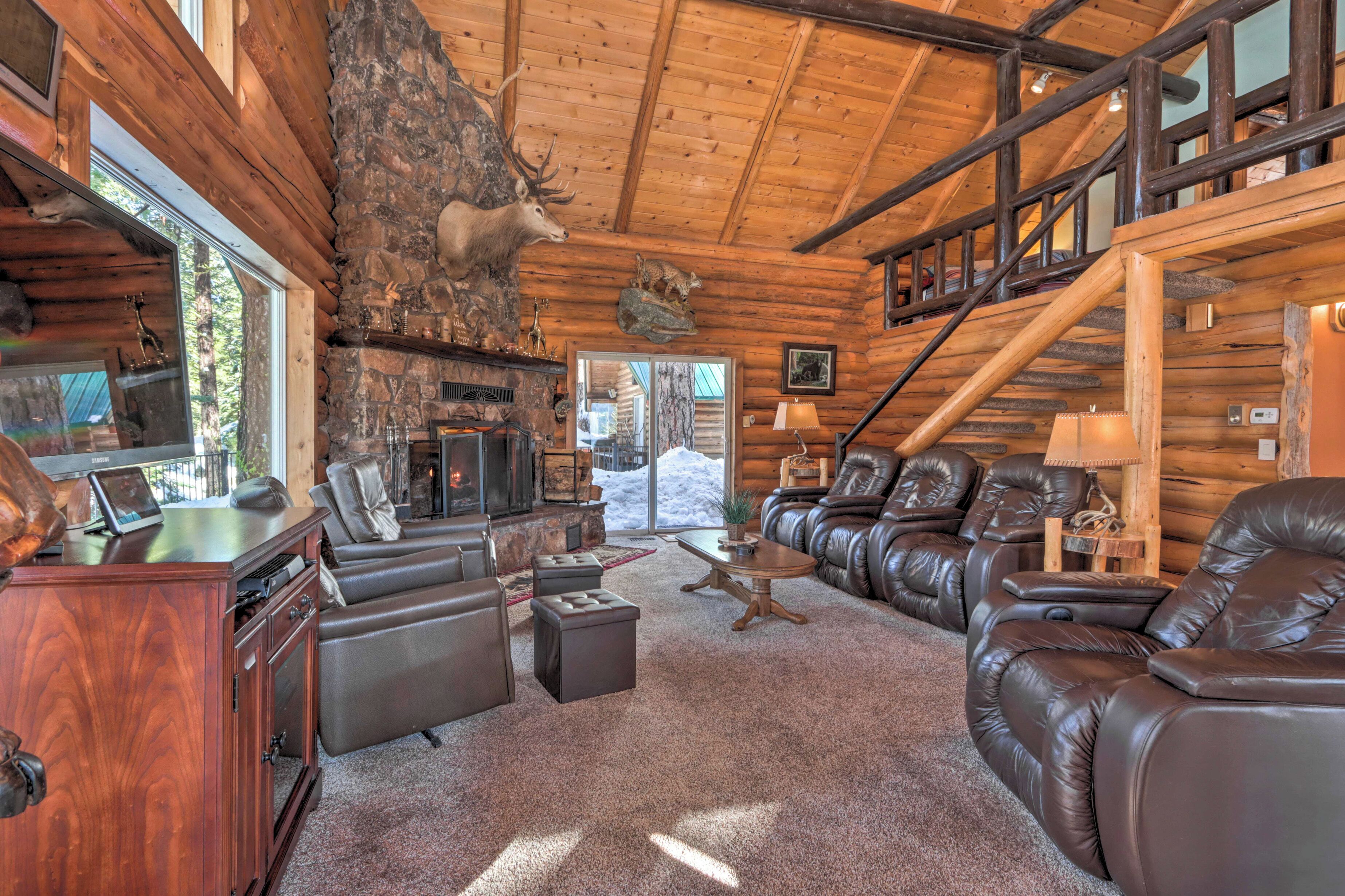 A log cabin interior with a stone fireplace, leather furniture, and a deer mounted on the wall.