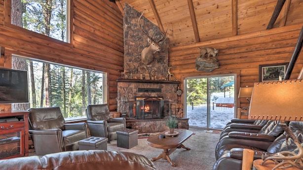 A log cabin interior with a stone fireplace, leather furniture, and a large window overlooking a snowy landscape. - Cascade Cabin w/ Mountain View & River Access (Cascade)