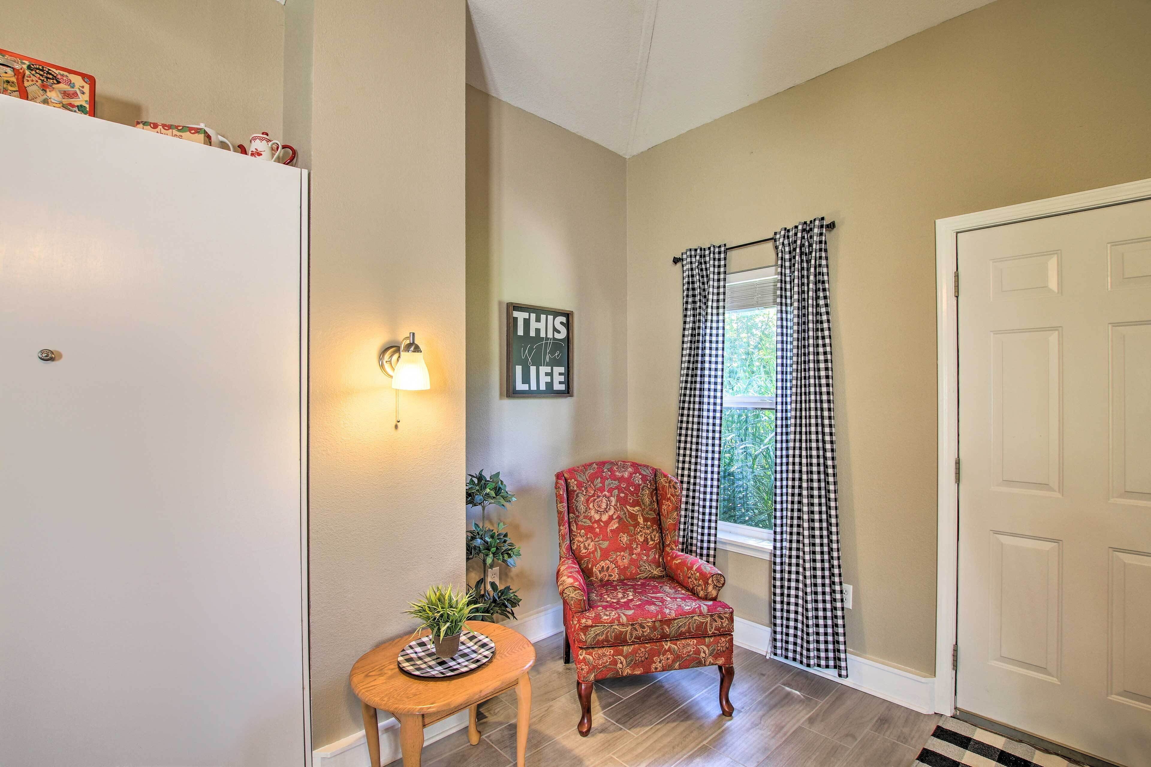 A hallway with a checkered curtain, a floral armchair, a small table with a plant, and a wall-mounted light fixture.
