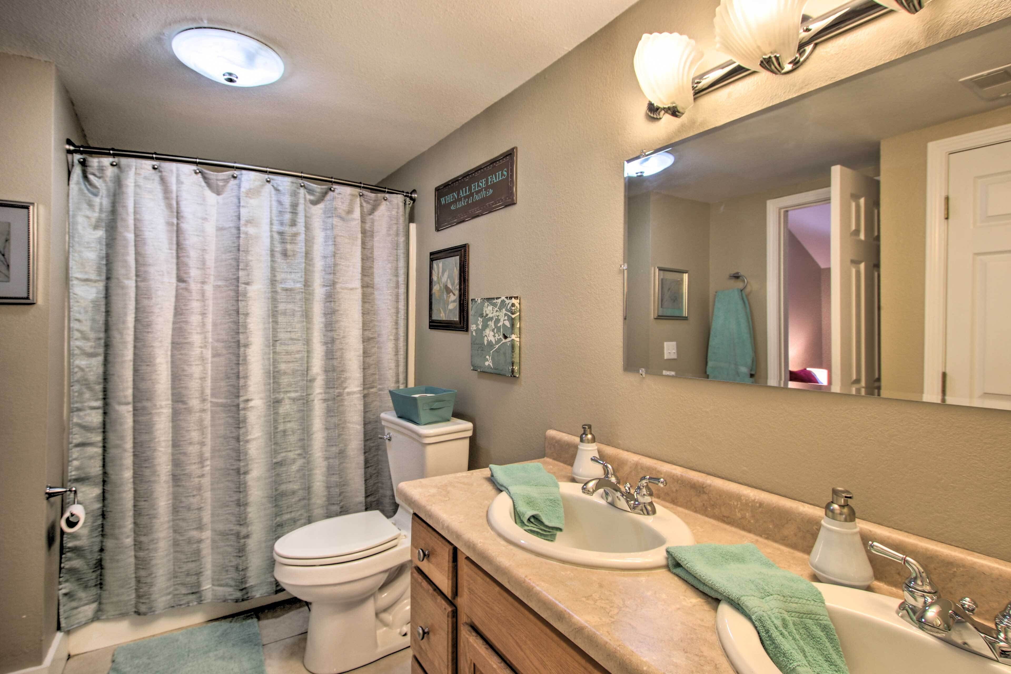 A bathroom with a shower curtain, toilet, sink, and vanity.