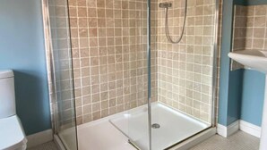 Een douche met een glazen deur, betegelde wanden en een witte vloer.