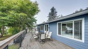 A deck with a table and chairs, overlooking a blue house with large windows. - Lakefront Mount Vernon Home w/ Private Dock! (Sedro-Woolley)