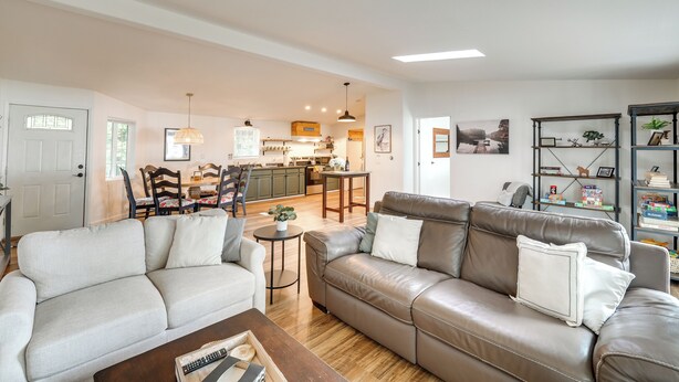 A spacious living room with a brown leather sofa, a grey sofa, and a wooden coffee table. There is a kitchen in the background with a bar and a dining area. - Lakefront Mount Vernon Home w/ Private Dock! (Sedro-Woolley)