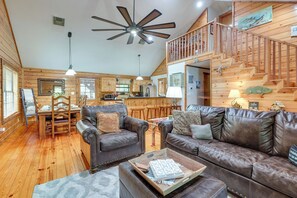 A spacious living area with a wooden ceiling fan, a dining table with chairs, a brown leather sofa, and a staircase leading to an upper level. - 'cape Royale' Luxury Livingston Cabin w/ Hot Tub! (Coldspring)