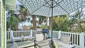 Une terrasse extérieure couverte, équipée d’un barbecue, de sièges et d’un parasol à motifs.