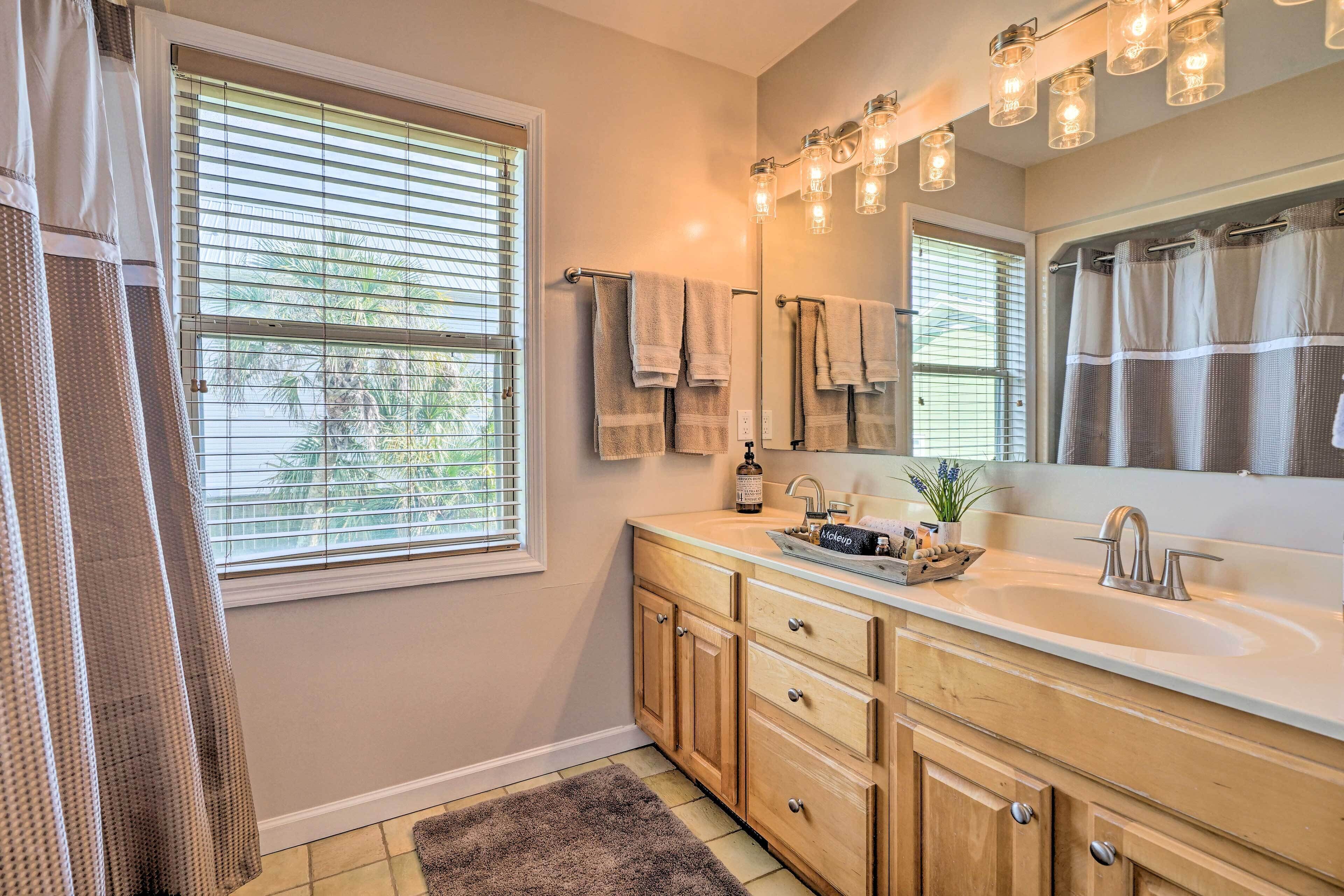 A bathroom with a double sink, wooden cabinets, a large mirror, and a window with blinds.