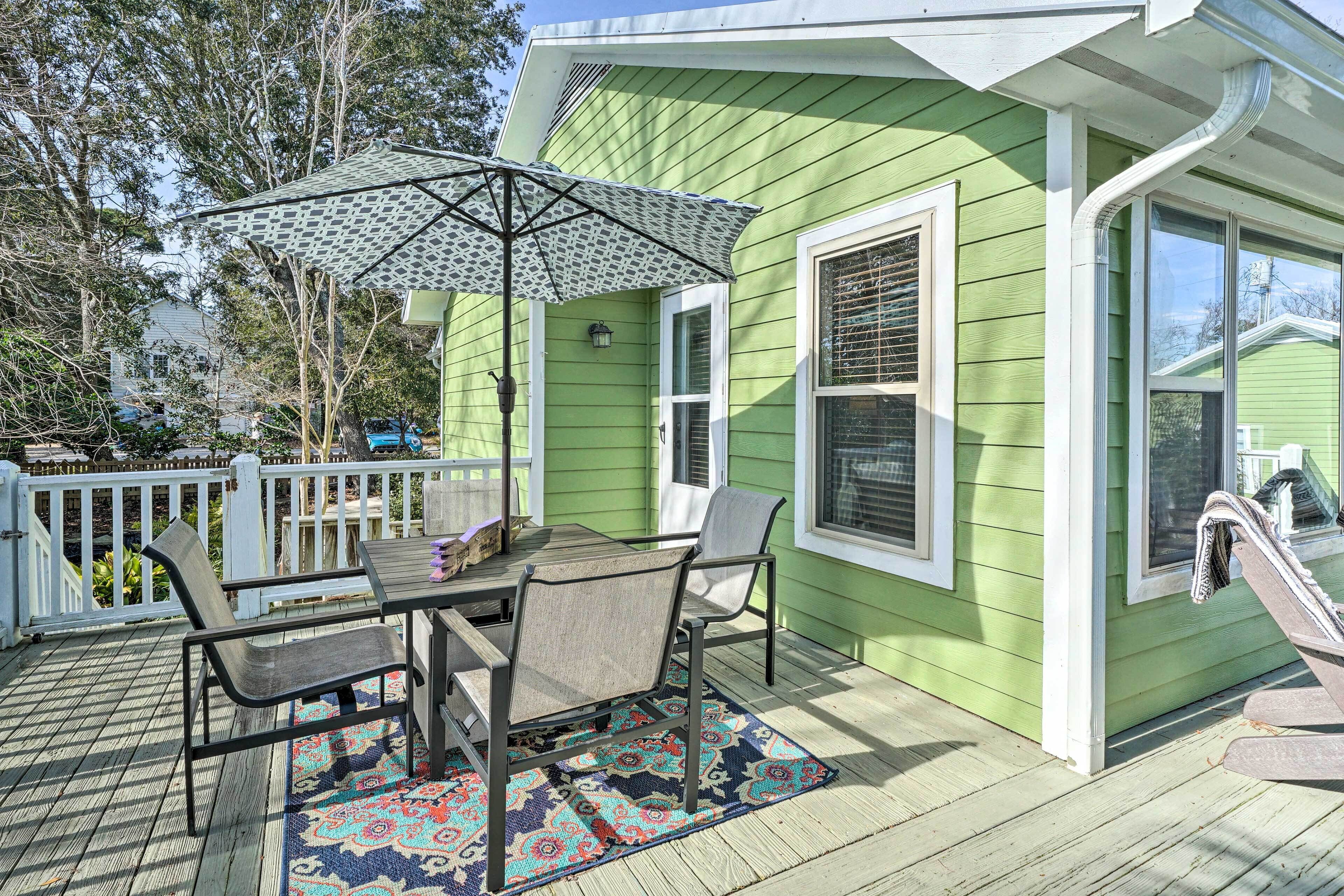 Une maison verte avec un patio couvert, une table avec des chaises et un tapis à motifs.