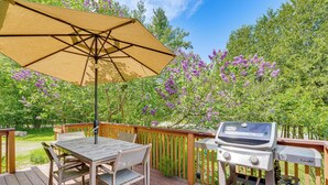 Une terrasse en bois avec une table et des chaises, un barbecue et un parasol.