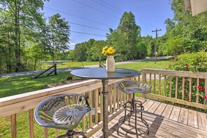 A wooden deck with metal chairs and a table, surrounded by lush greenery and a clear sky. - 'the Country Cottage in Union Mills w/ Porch! (Union Mills)
