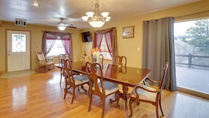 A dining area with a large wooden table, six chairs, a chandelier, and a view through a large window. - Mtn-view Home w/ Deck, 2 Mi to Mickelson Trail! (Lead)