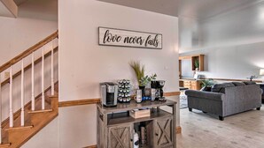 A living room with a staircase, a coffee station, a grey sofa, and a motivational sign on the wall. - Peaceful Bird in Hand Home w/ Farmland Views! (Bird In Hand)