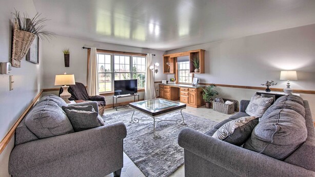 A living room with a sofa set, a glass coffee table, a TV, and a kitchen area with cabinets and a sink. - Peaceful Bird in Hand Home w/ Farmland Views! (Bird In Hand)