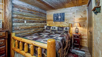 A log cabin bedroom with a wooden bed, a quilt, a nightstand, and a lamp.