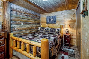 A log cabin bedroom with a wooden bed, a quilt, a nightstand, and a lamp. - Arkdale Studio Cabin w/ On-site ATV Trails! (Arkdale)