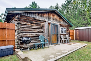 A rustic cabin with a wooden exterior, a front door, a window, and a patio area with outdoor seating. - Arkdale Studio Cabin w/ On-site ATV Trails! (Arkdale)
