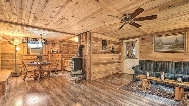 L’intérieur d’une cabane en rondins comprend un coin repas, un poêle à bois, un canapé et un ventilateur de plafond.