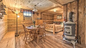 L’intérieur chaleureux d’un chalet avec des murs en bois, un coin repas avec des chaises, un canapé et un poêle d’époque.